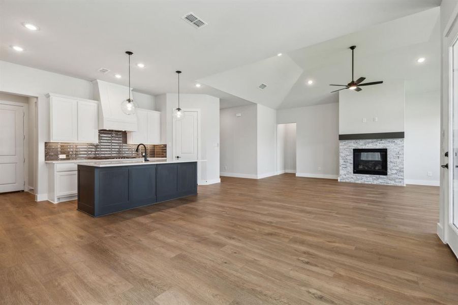 Kitchen featuring a center island with sink, hanging light fixtures, white cabinetry, and light hardwood / wood-style flooring