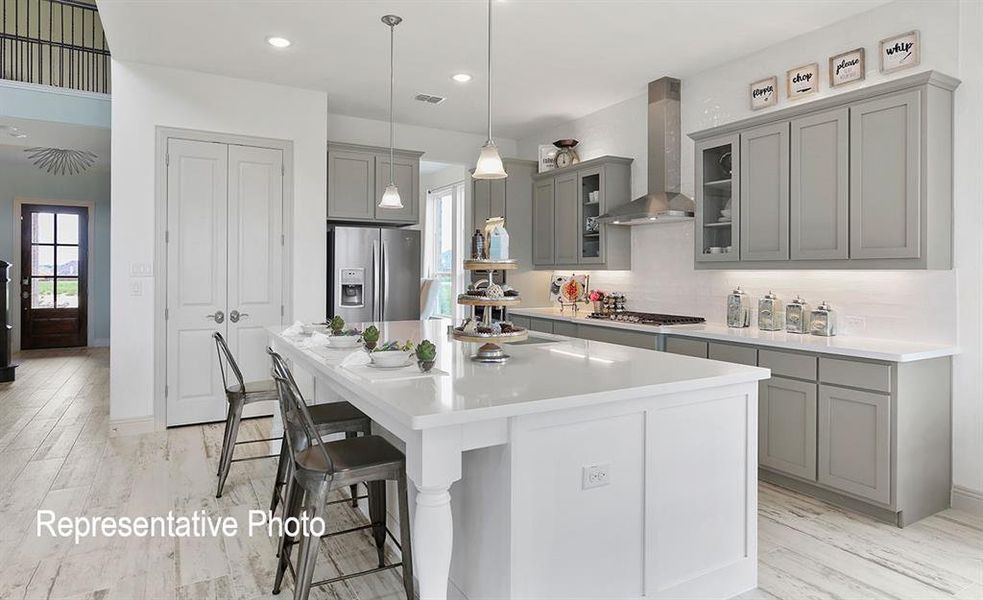 Gourmet kitchen featuring a large central island with seating, grey cabinetry, stainless steel appliances, and wood-finish flooring