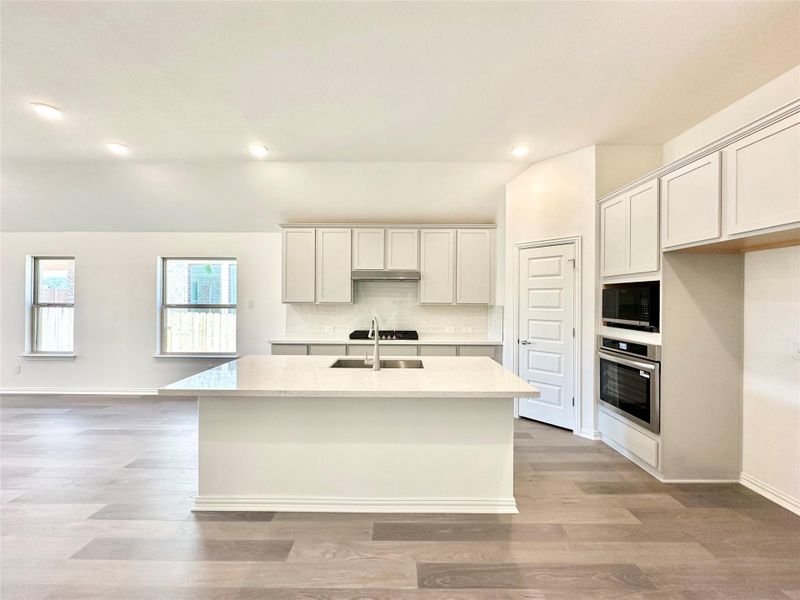 Kitchen with backsplash, a kitchen island with sink, stainless steel oven, light stone counters, and recessed lighting
