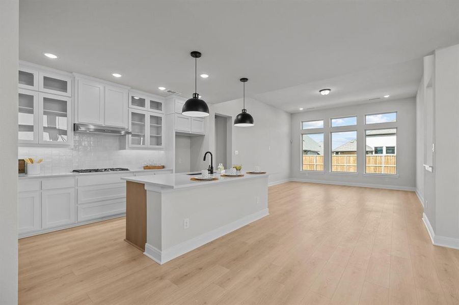 Modern kitchen featuring white cabinetry with glass-front accents, white subway tile backsplash, and stainless steel range hood Modern kitchen featuring white cabinetry with glass-front accents, white subway tile backsplash, and stainless steel range hood