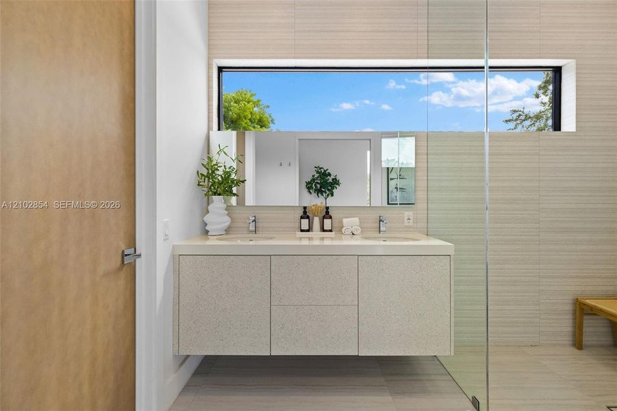 Floating dual-sink vanity with a speckled countertop, wide-format horizontal wall tiling, rectangular clerestory window, and seamless glass shower enclosure