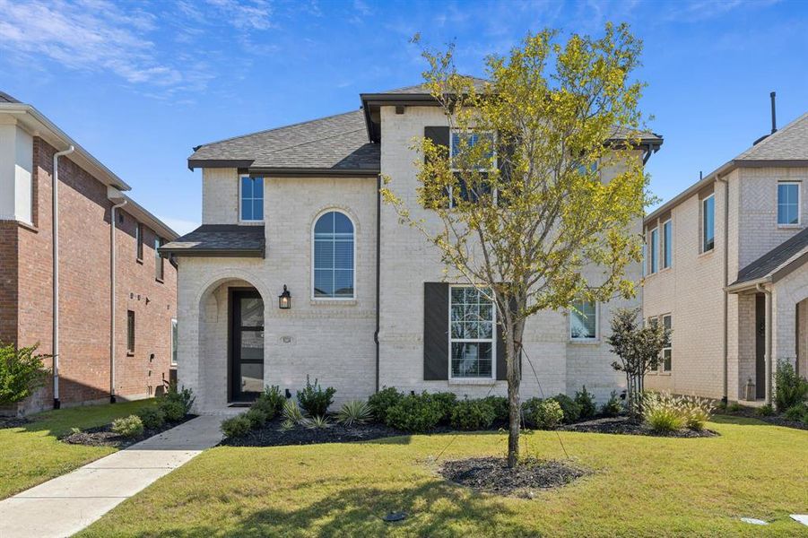 French country home with brick siding, a front yard, and a shingled roof French country home with brick siding, a front yard, and a shingled roof
