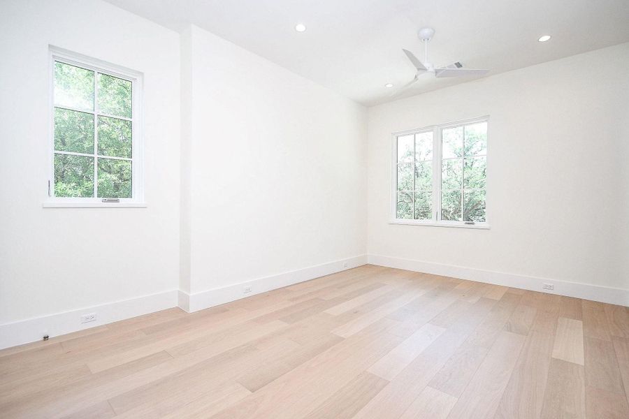 Bright, spacious room with light wood flooring, neutral walls, and large windows allowing plenty of natural light. Features a ceiling fan and recessed lighting.
