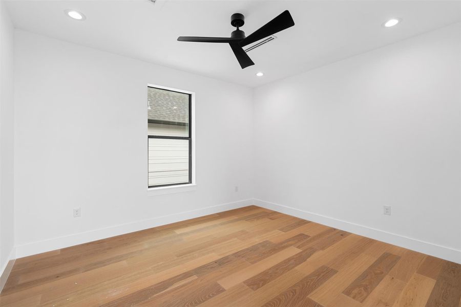 This room features light hardwood flooring, a modern black ceiling fan, and recessed lighting