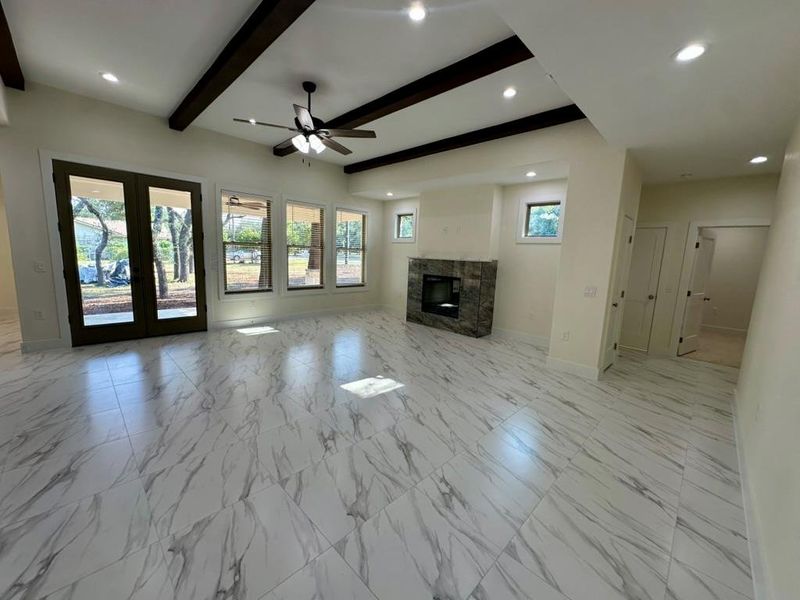 Unfurnished living room with beam ceiling, recessed lighting, light marble finish floors, a glass covered fireplace, and french doors