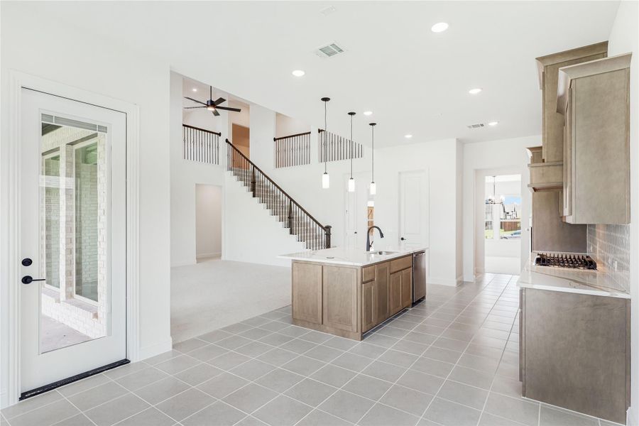Open kitchen with center island, pendant lights, wood cabinets, and tile floors, open to staircase and living area