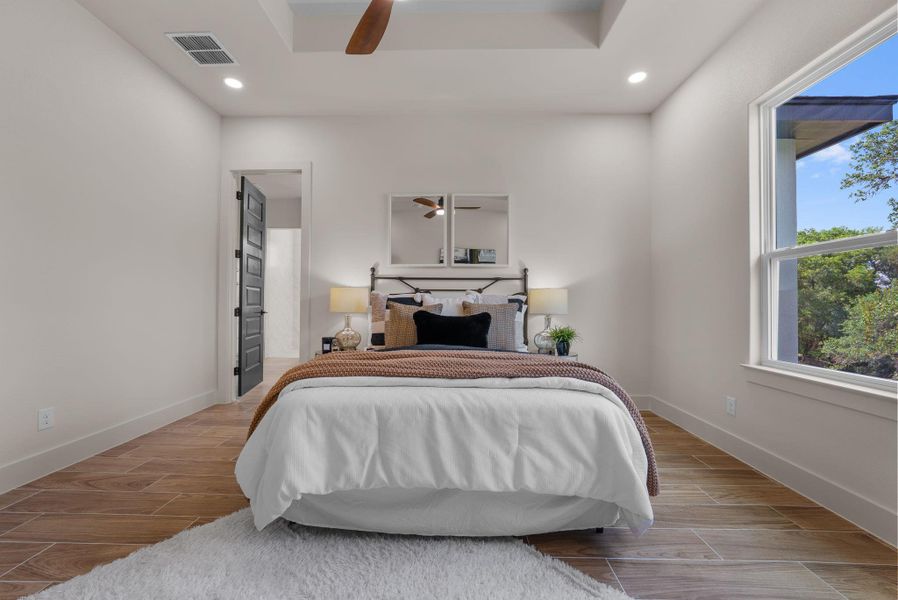 A tranquil primary bedroom with a soaring tray ceiling and durable tile flooring, perfect for unwinding.