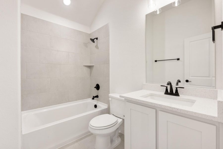 Full bathroom with white tiled tub-shower combo, white vanity with quartz countertop, and black fixtures