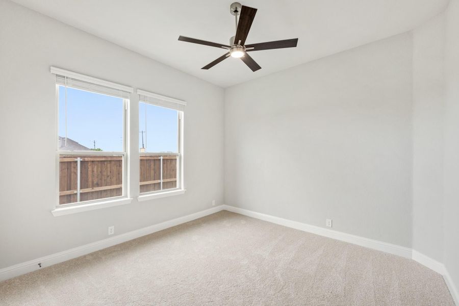 Empty bedroom with carpet flooring, ceiling fan, and two windows with natural light