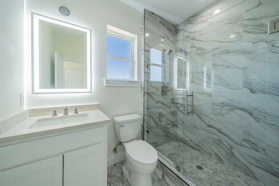 Full bath with vanity, a marble finish shower, a textured wall, and light marble finish floors Full bath with vanity, a marble finish shower, a textured wall, and light marble finish floors
