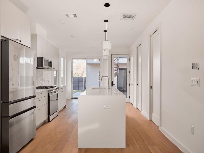 Kitchen with stainless steel appliances, white cabinets, decorative light fixtures, tasteful backsplash, and light wood-type flooring