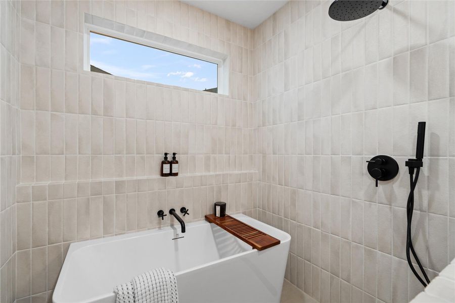 Tucked beneath a picture window and surrounded by floor-to-ceiling tile, this freestanding tub offers a luxurious escape within the walk-in wet room. Matte black fixtures and spa-style detailing create a serene, high-design space where you can unwind in total tranquility.