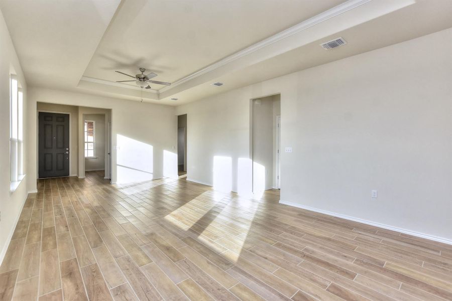 Unfurnished room with visible vents, a ceiling fan, a tray ceiling, baseboards, and wood tiled floor