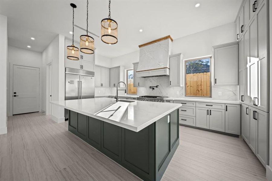 This luxury kitchen is a chef’s dream, featuring a grand quartz island with seating, custom cabinetry, and high-end stainless steel appliances. The unique vent hood with marble detail and warm wood accents adds a touch of elegance, while the pendant lighting creates a stylish focal point. With its thoughtful design and premium finishes, this kitchen seamlessly combines beauty and functionality, perfect for culinary enthusiasts and entertainers alike.