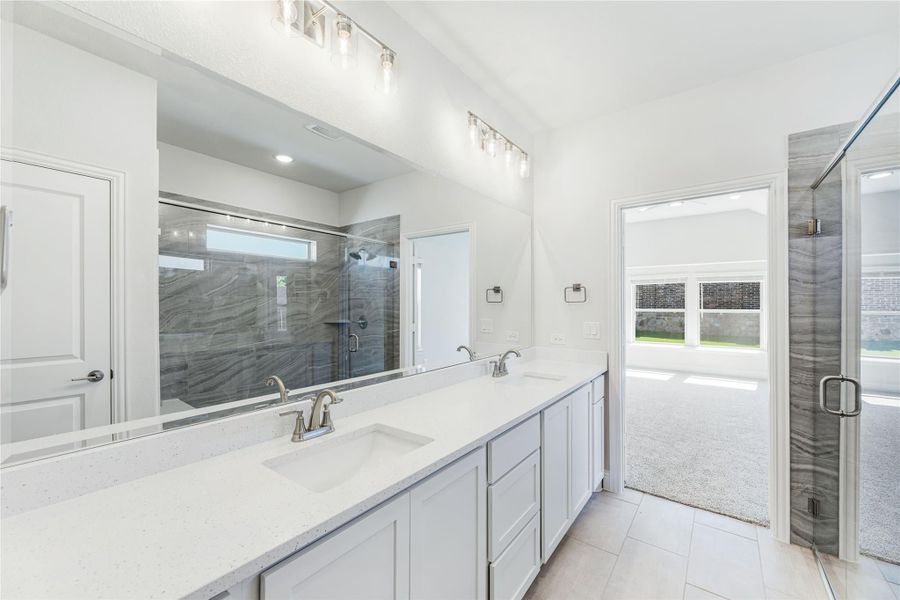 Master bathroom with double sink vanity, quartz countertop, large mirror, and glass-enclosed shower with gray tile walls.