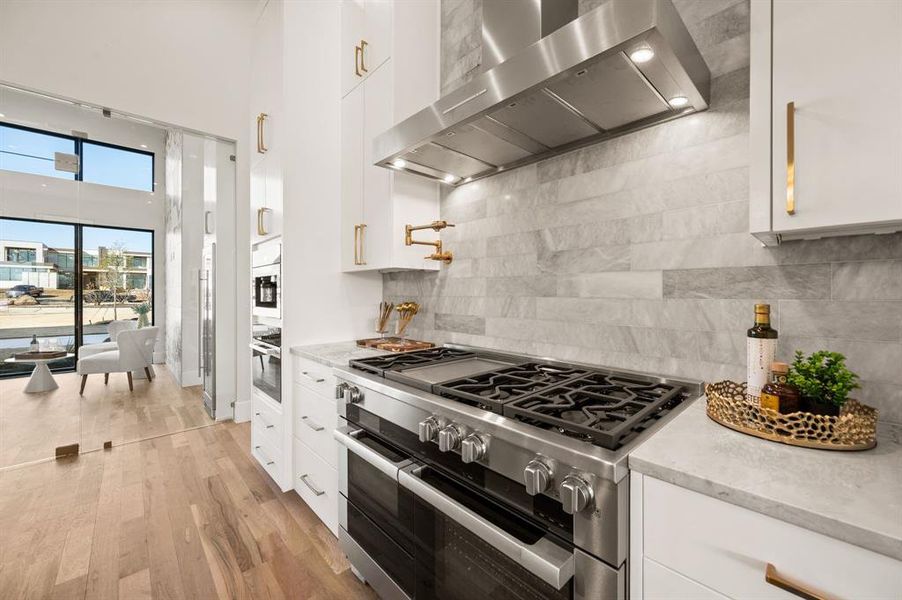 Kitchen featuring appliances with stainless steel finishes, range hood, backsplash, white cabinets, and light hardwood / wood-style floors