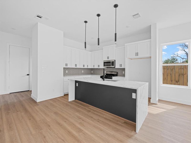 This photo showcases a bright, open-concept living space featuring a modern kitchen with a sleek marble countertop and black fixtures. The area has light wood flooring, ample natural light from large windows, and a door leading to a fenced backyard, creating a seamless indoor-outdoor flow.