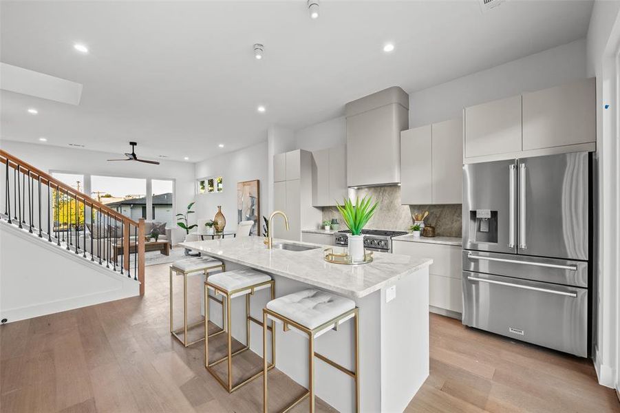 Kitchen featuring stainless steel appliances, light wood-type flooring, light stone counters, an island with sink, and a breakfast bar area