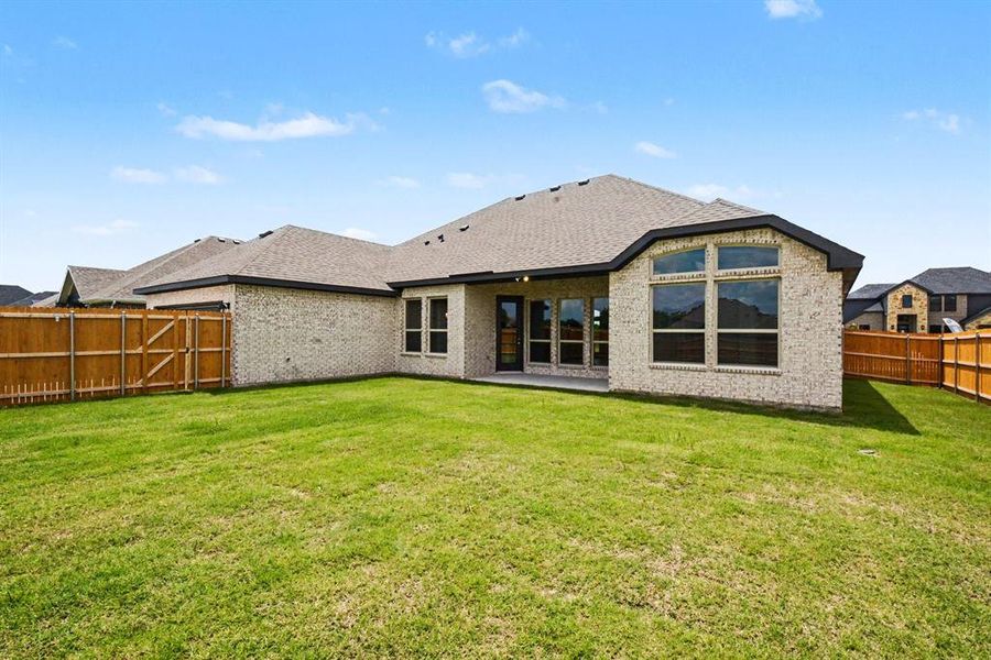 Expansive backyard featuring a manicured lawn, full wood fencing, a covered concrete patio, and a light-toned brick exterior with large windows Expansive backyard featuring a manicured lawn, full wood fencing, a covered concrete patio, and a light-toned brick exterior with large windows