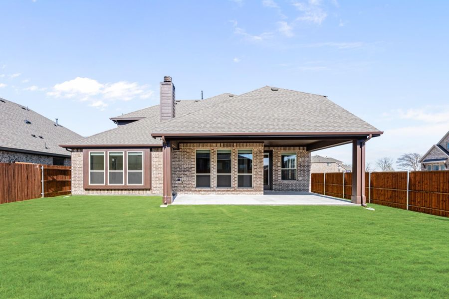 Brick home rear exterior with covered patio, green lawn, and wood privacy fence