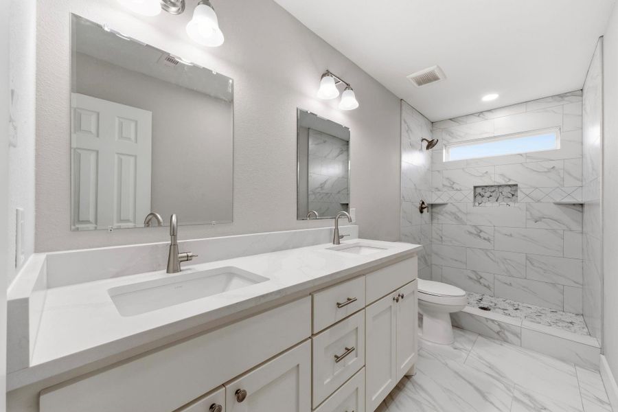 Spa inspired primary bath features dual sinks, quartz countertops, a floor to ceiling ceramic tile shower, and a built in shower niche.