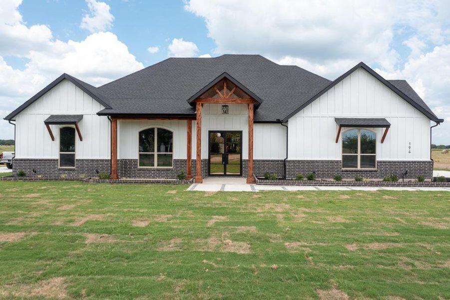 Modern farmhouse style home with board and batten siding, a front yard, and roof with shingles