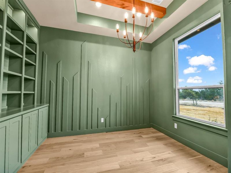 Empty room with a chandelier, light hardwood / wood-style floors, and a raised ceiling