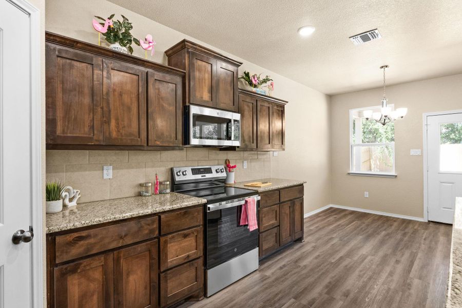 Kitchen featuring appliances with stainless steel finishes, decorative backsplash, dark brown cabinetry, light stone countertops, and dark wood-style flooring