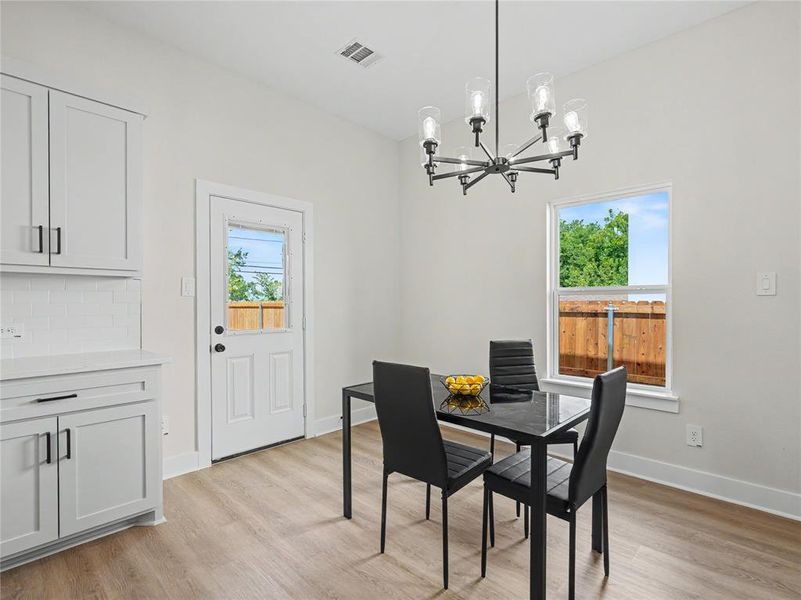 Bright interior featuring white walls, wood-finish flooring, white cabinetry with dark pulls, white subway tile backsplash, and a modern dark metal chandelier Bright interior featuring white walls, wood-finish flooring, white cabinetry with dark pulls, white subway tile backsplash, and a modern dark metal chandelier