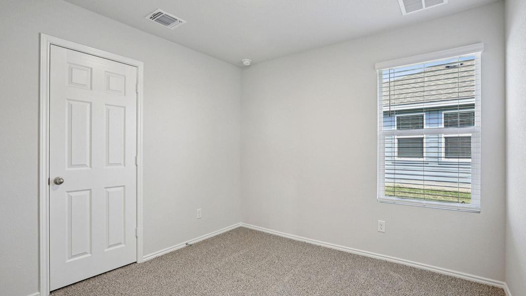 A well-lit secondary bedroom provides ample natural light and plush carpeting.