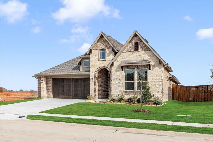 Single-story home with stone and brick exterior, arched entry, two-car garage, and green front lawn Single-story home with stone and brick exterior, arched entry, two-car garage, and green front lawn