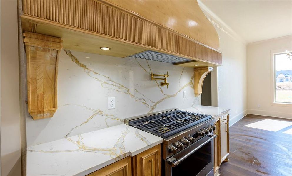 Kitchen with high end stainless steel range, light stone countertops, dark wood-type flooring, wood finish cabinetry, and ornamental molding