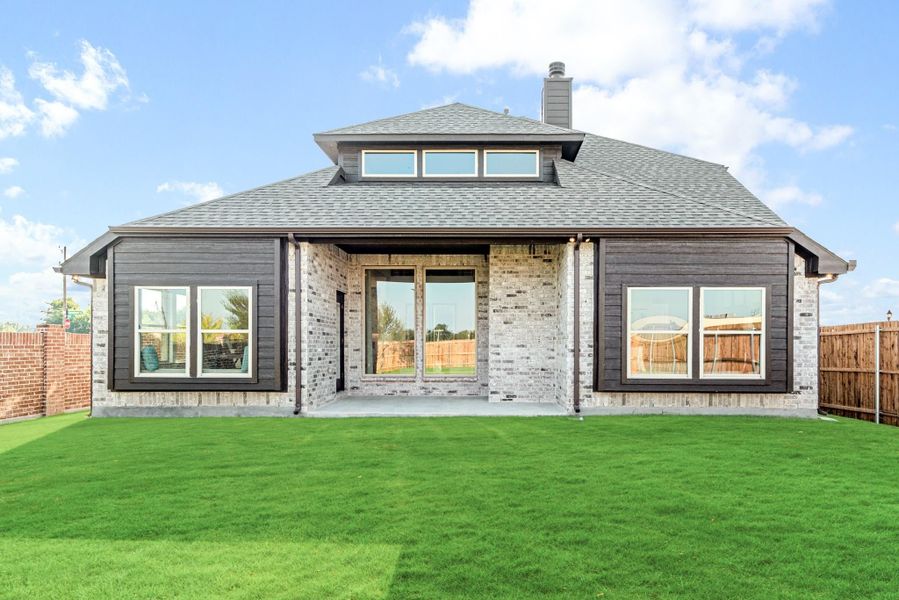 Rear exterior of single-story home with brick and dark siding, covered patio, large windows, and green backyard lawn. Rear exterior of single-story home with brick and dark siding, covered patio, large windows, and green backyard lawn.