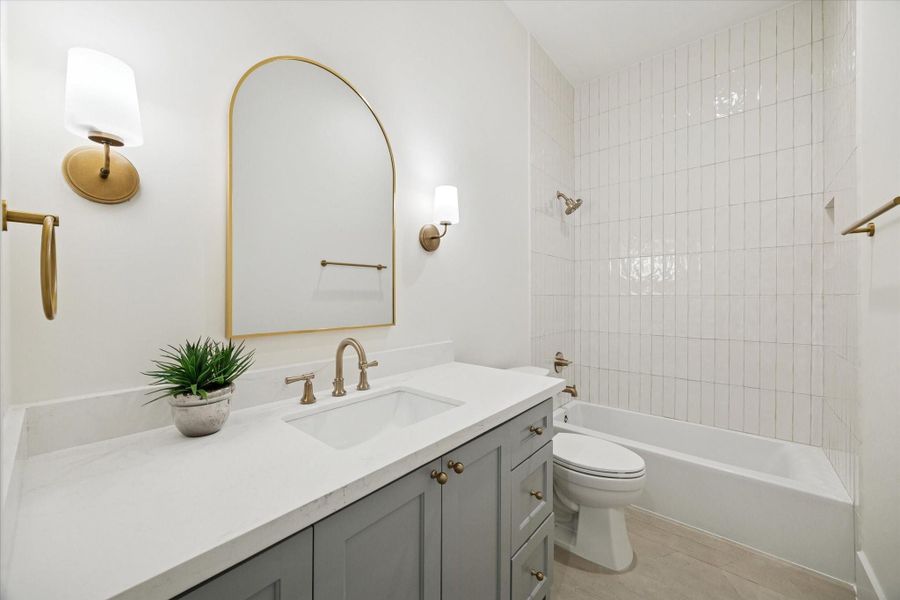 Guest bath with quartz vanity, shower / tub combination, stylish tile, and modern fixtures.