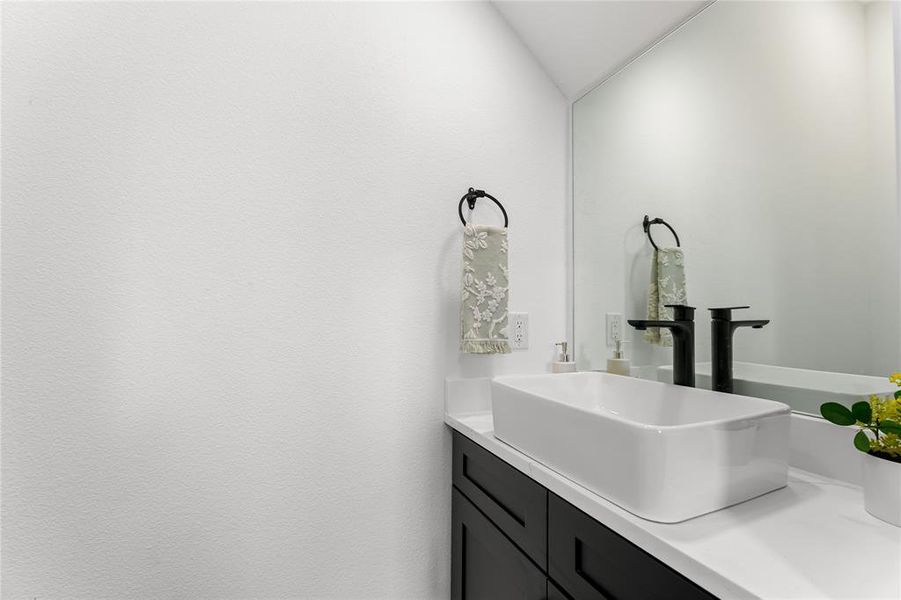 Vanity featuring a rectangular vessel sink, black cabinetry, white countertop, and a wall-mounted mirror