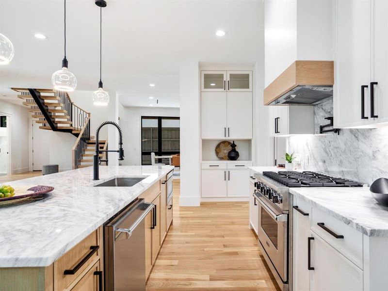 Two tone kitchen featuring light stone counters, pendant lighting, stainless steel appliances, light wood finished floors, and glass insert cabinets