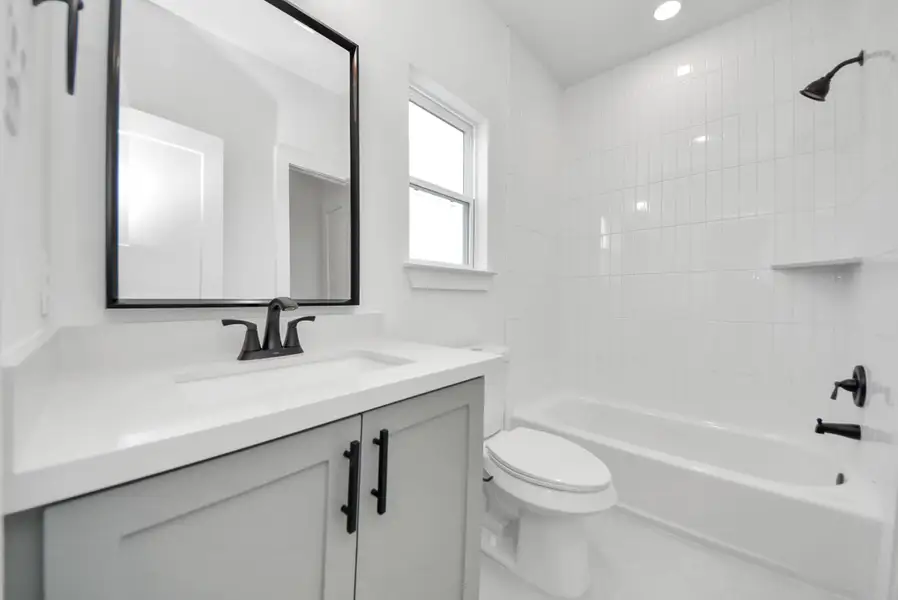 This modern bathroom features a sleek vanity with a large mirror, a bathtub surrounded by white tile, and a window that brings in natural light, creating a bright and welcoming atmosphere.