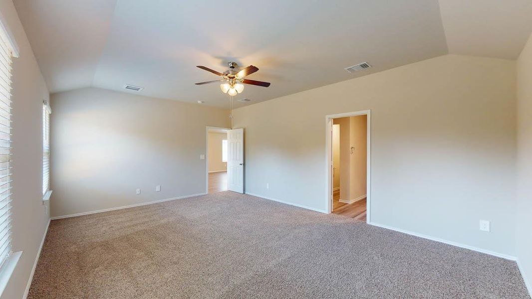 A spacious, naturally illuminated room featuring vaulted ceilings and a practical ceiling fan.