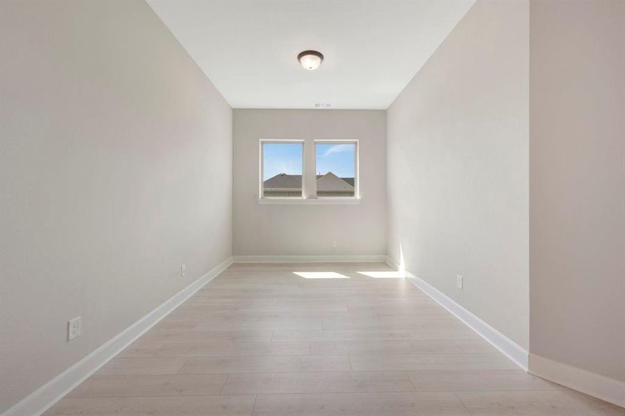 Neutral-toned room featuring light wood-finish flooring, white baseboards, and dual windows with white framing