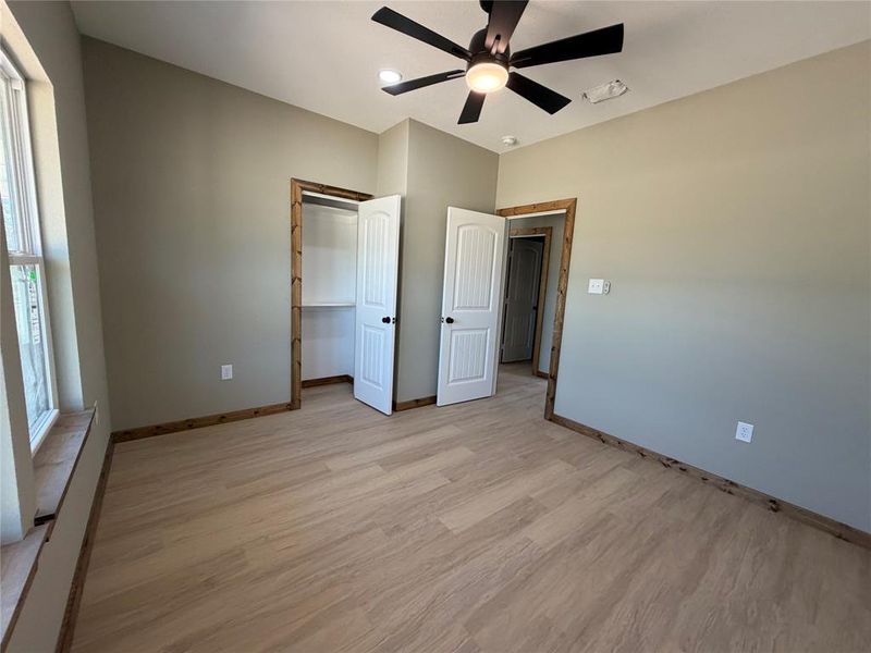 Spacious bedroom featuring wood-finish flooring, a ceiling fan with integrated lighting, and multiple doors with wood trim