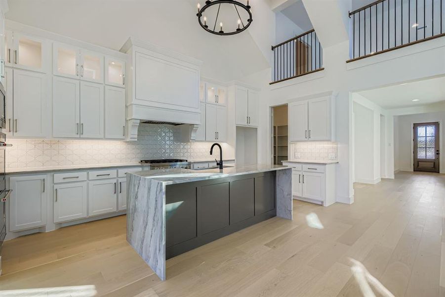 Kitchen with backsplash, light stone counters, white cabinets, a kitchen island with sink, and light wood-style flooring