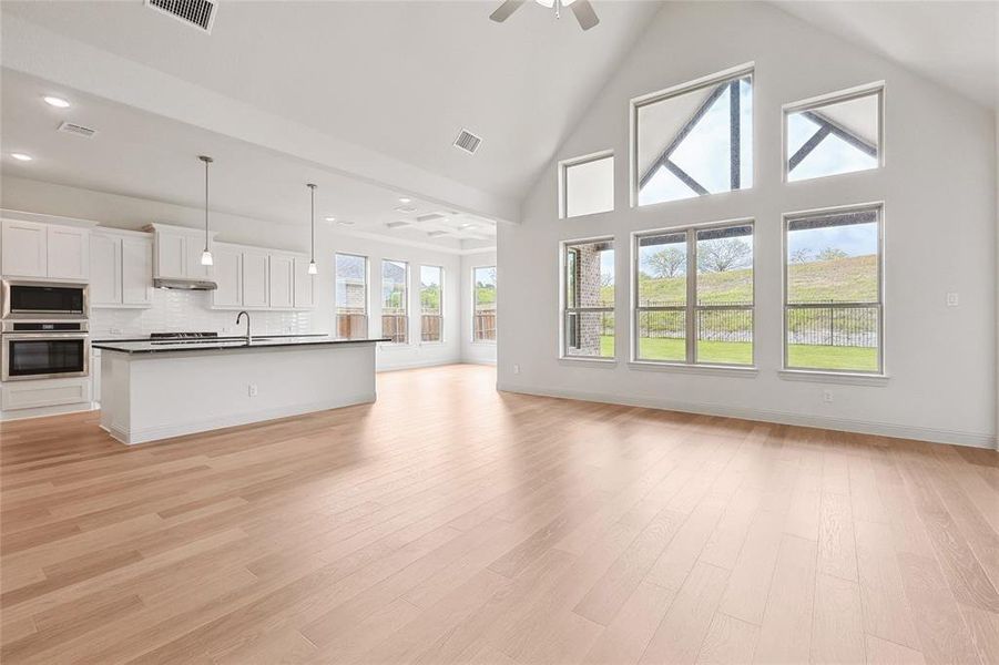 Unfurnished living room with high vaulted ceiling, sink, light wood-type flooring, and ceiling fan