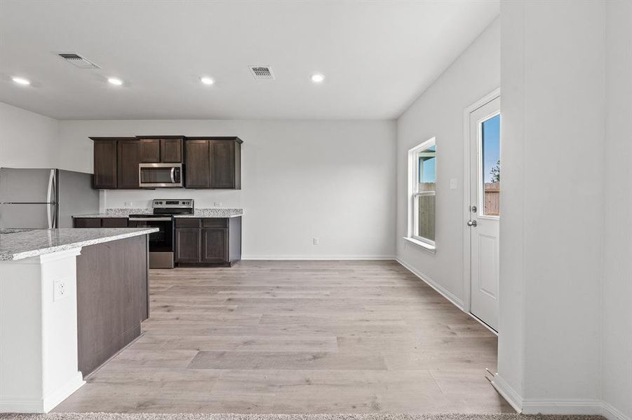 Kitchen with dark brown cabinetry, light stone countertops, stainless steel appliances, and light wood-type flooring