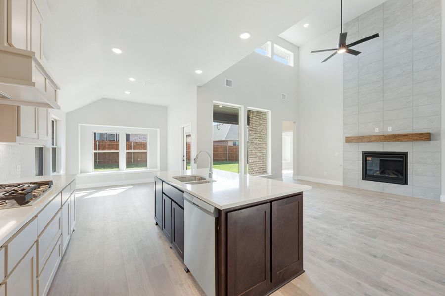 Open kitchen with dark island, white countertops, high vaulted ceiling, and tile fireplace in adjacent living area