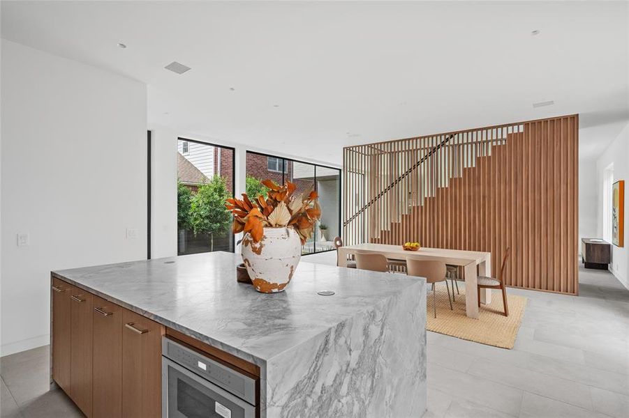 This bright, airy kitchen is flooded with natural light, highlighting the sleek custom cabinetry that features soft-close drawers for a smooth, modern touch. The expansive island and countertops are equipped with hidden in-counter outlets, offering a clean and functional design.