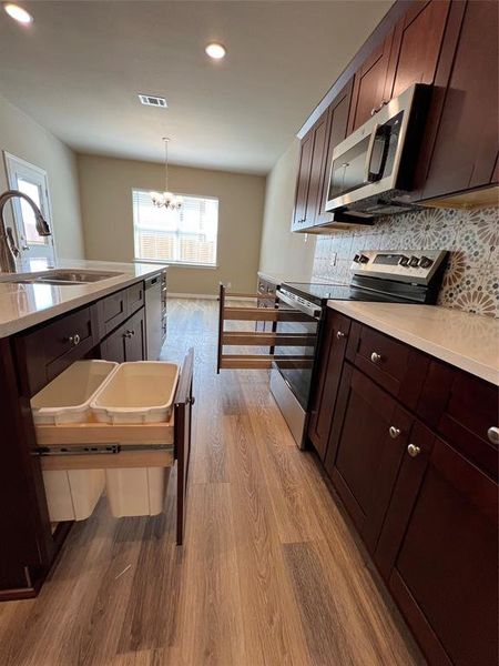 Kitchen with pendant lighting, stove, light hardwood / wood-style flooring, sink, and a notable chandelier