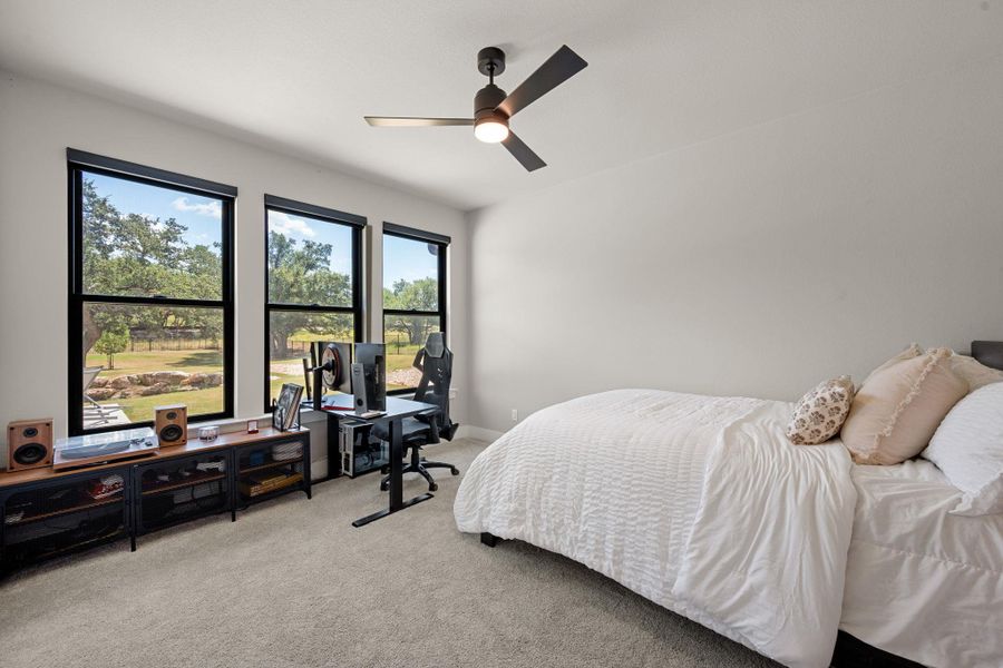 Generous windows frame peaceful backyard views in this carpeted bedroom.