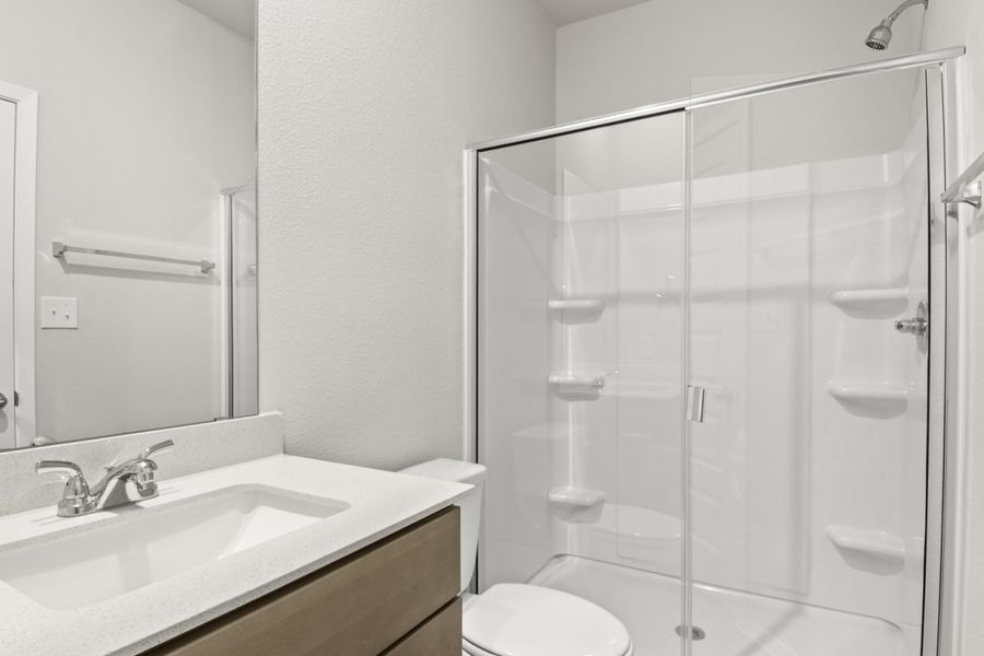 Image of a primary bathroom with brown cabinets, a white vanity and a walk-in shower