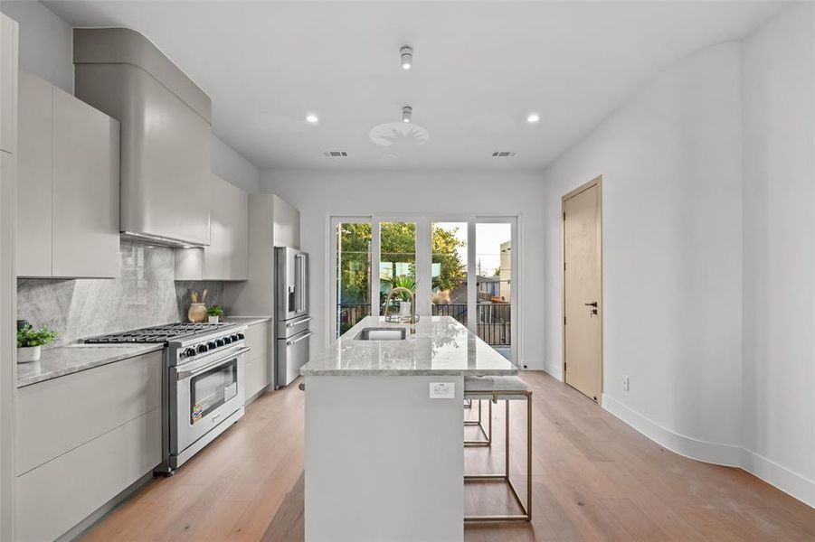 Kitchen with an island with sink, light stone counters, stainless steel appliances, light wood-type flooring, and decorative backsplash