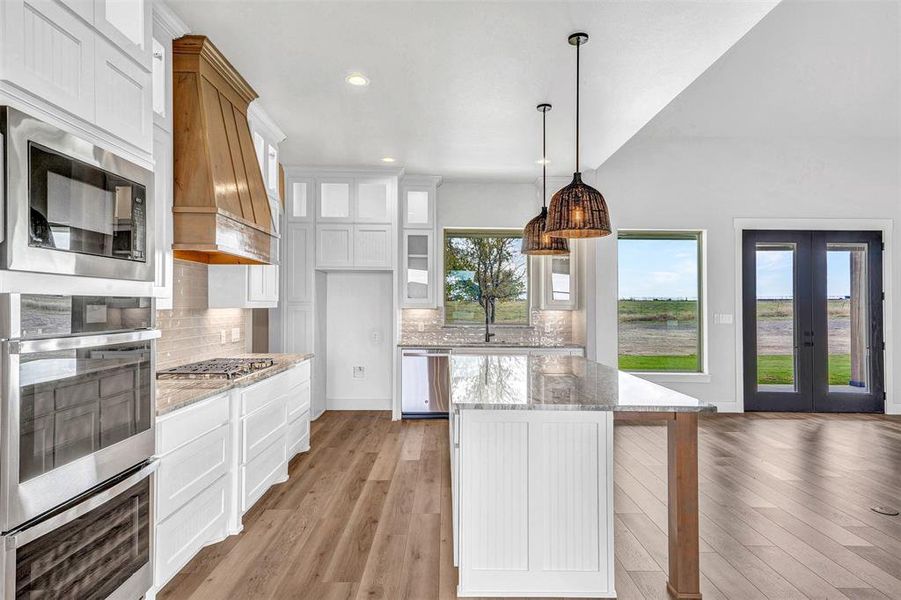 Kitchen with premium range hood, white cabinetry, light stone counters, and light wood-type flooring